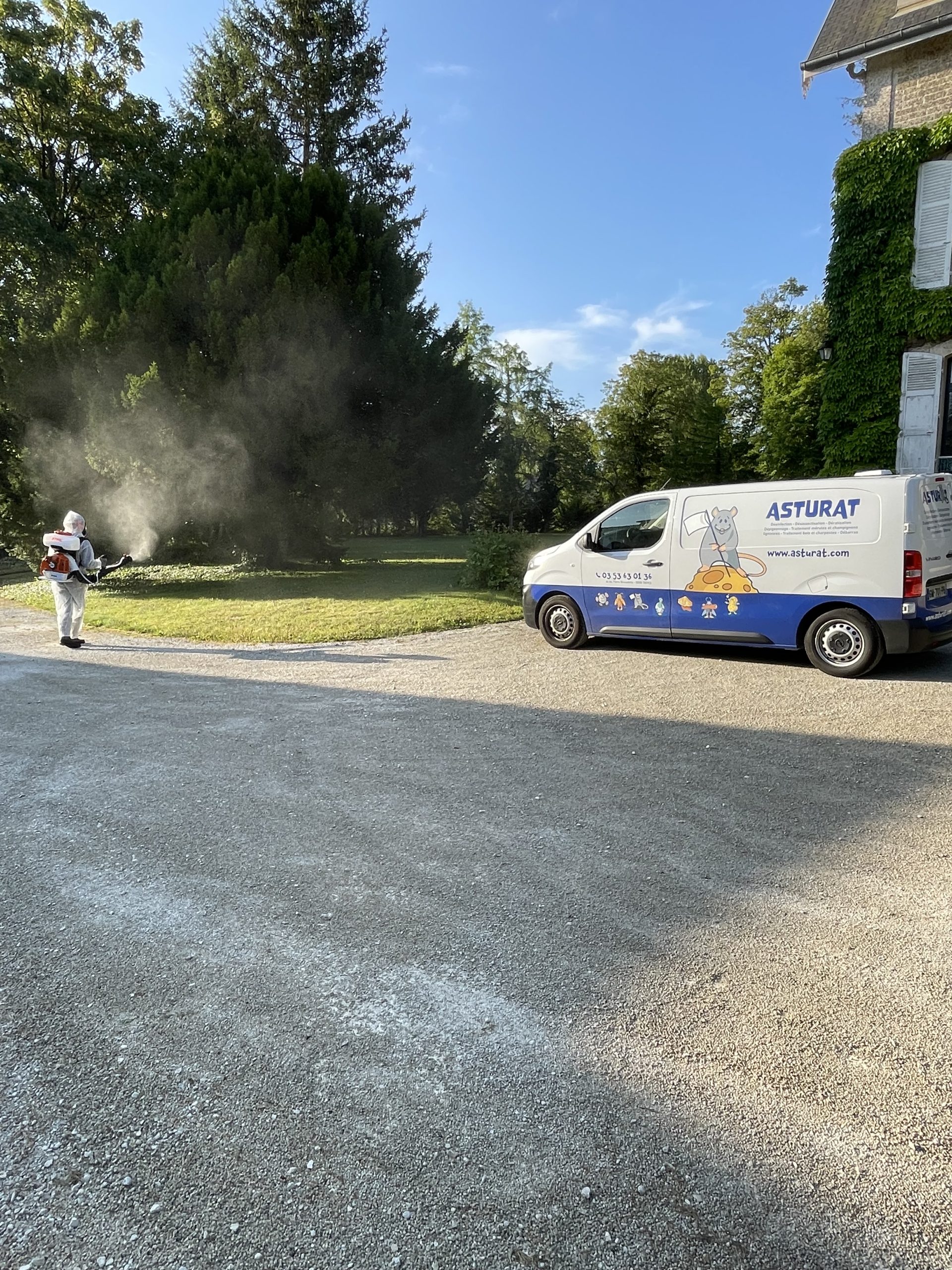 Technicien Asturat en combinaison effectuant un traitement anti-moustiques en jardin